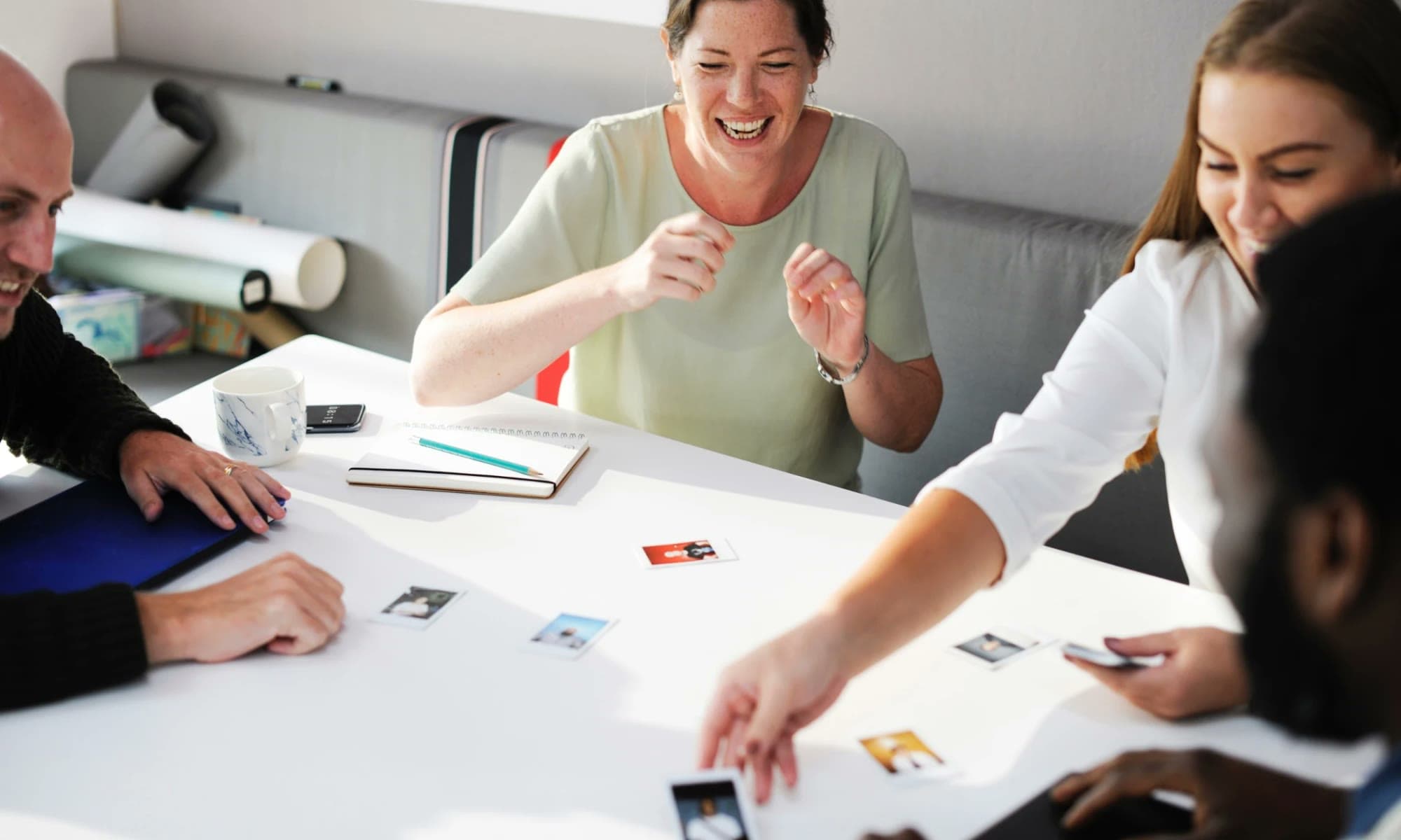 A group reviewing headshot-style photos laid out on a table, laughing together